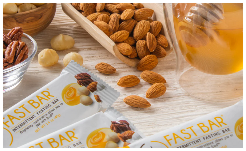 Barrette Prolon Honey & Nut Fast esposte su un tavolo con miele, mandorle, noci pecan e altra frutta secca